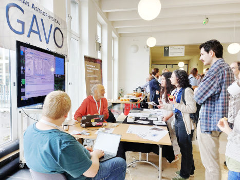 People standing an sitting around a booth-like table.  There's a big GAVO logo and a big screen on the left-hand side, a guy in a red hoodie is clearly giving a demo.