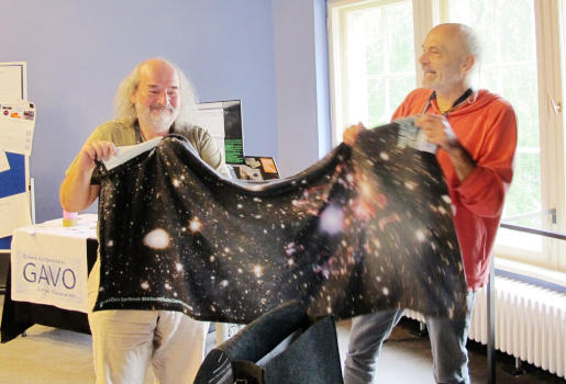 Two persons holding a large towel with an astronomical image on it.