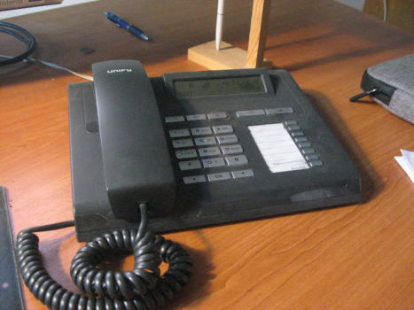 A business phone with many custom buttons on a moderately cluttered desk